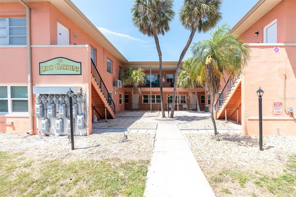 The exterior of a two-story peach-colored apartment complex features a central courtyard and palm trees — 121 46TH AVENUE UNIT 1G, ST PETE BEACH, FL