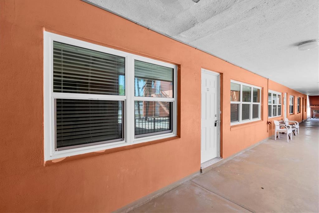 An exterior view of an orange building with a covered walkway, windows, and white doors — 121 46TH AVENUE UNIT 1G, ST PETE BEACH, FL