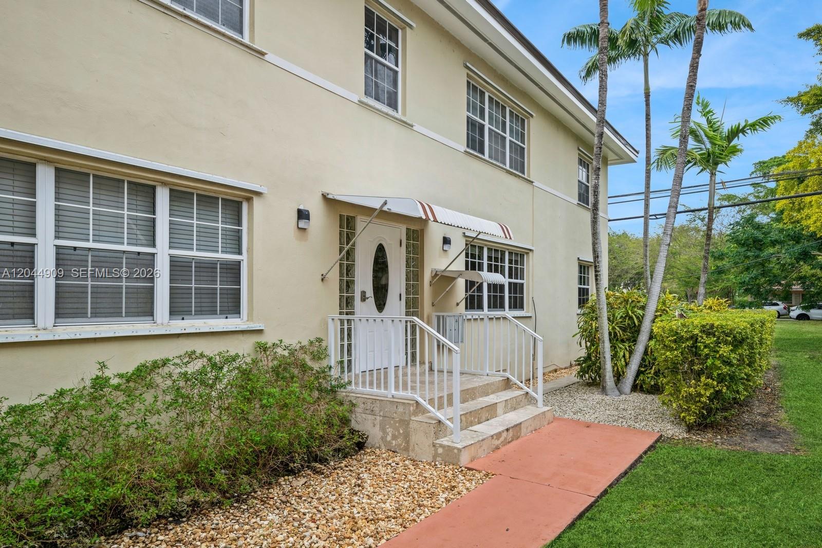 The exterior of a two-story beige building features a white front door and metal railings — 237 Madeira Ave # 3, Coral Gables FL 33134, CORAL GABLES, FL