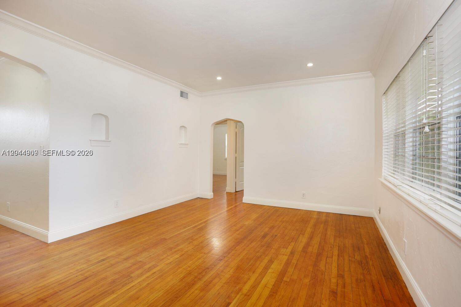 An empty room features hardwood floors, white walls, crown molding, and an arched doorway — 237 Madeira Ave # 3, Coral Gables FL 33134, CORAL GABLES, FL