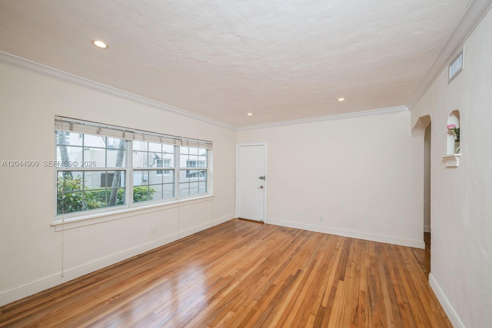 An empty room features hardwood floors, white walls, crown molding, and a large window — 237 Madeira Ave # 3, Coral Gables FL 33134, CORAL GABLES, FL