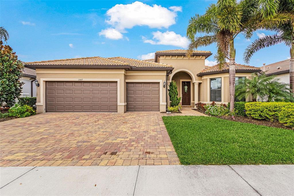 A single-story house with a tan stucco exterior, tile roof, and a paved driveway — 12437 GOLDEN SAGE DRIVE, SARASOTA, FL