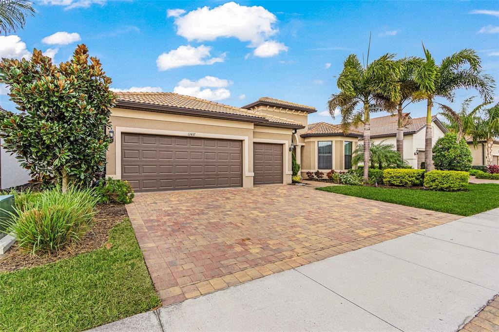 A single-story house with a tan exterior, brown garage doors, and a paved driveway — 12437 GOLDEN SAGE DRIVE, SARASOTA, FL