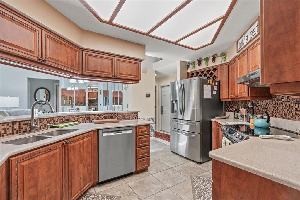 A kitchen with wood cabinets, stainless steel appliances, tile flooring, and a mosaic backsplash — 4 IPOMOEA COURT, HOMOSASSA, FL