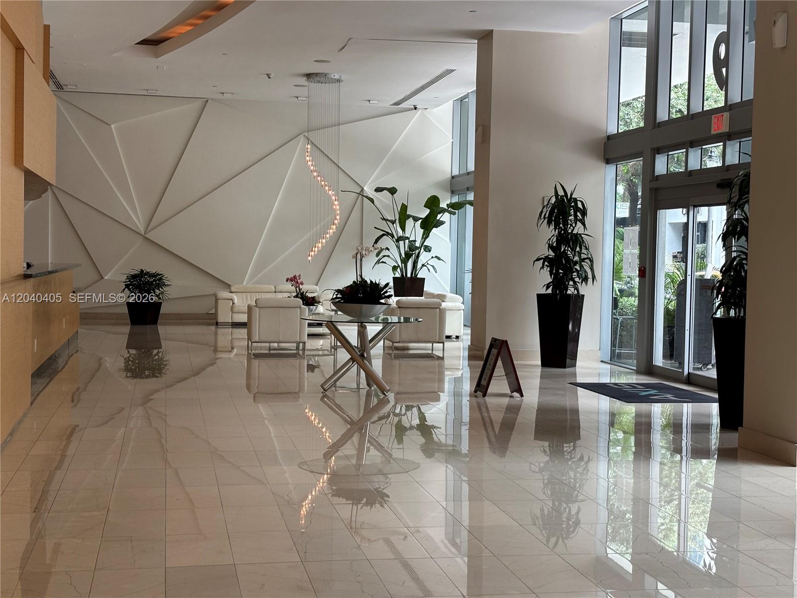 A modern building lobby features white geometric wall panels, polished tile floors, and contemporary furniture — 79 SW 12th St, Miami FL 33130, MIAMI, FL
