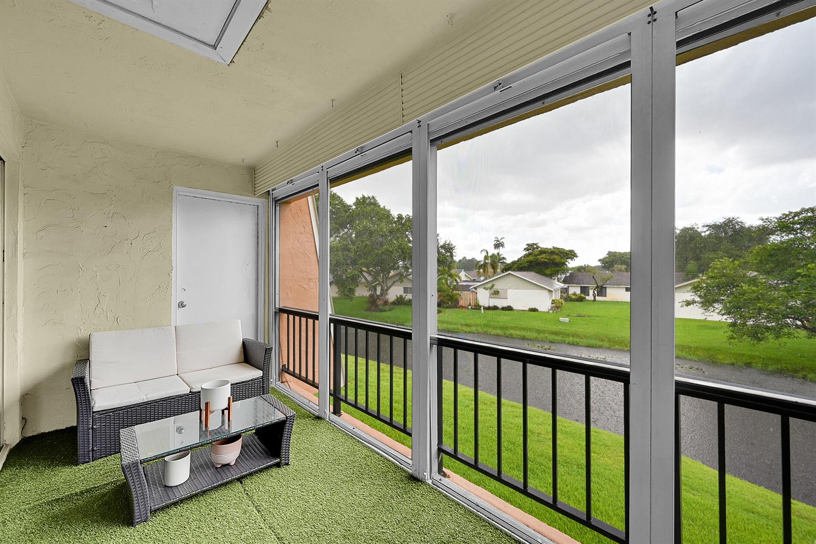 A screened-in balcony with artificial grass, patio furniture, and a view of a grassy lawn — 3630 Citrus Trace # 4, Davie FL 33328, DAVIE, FL