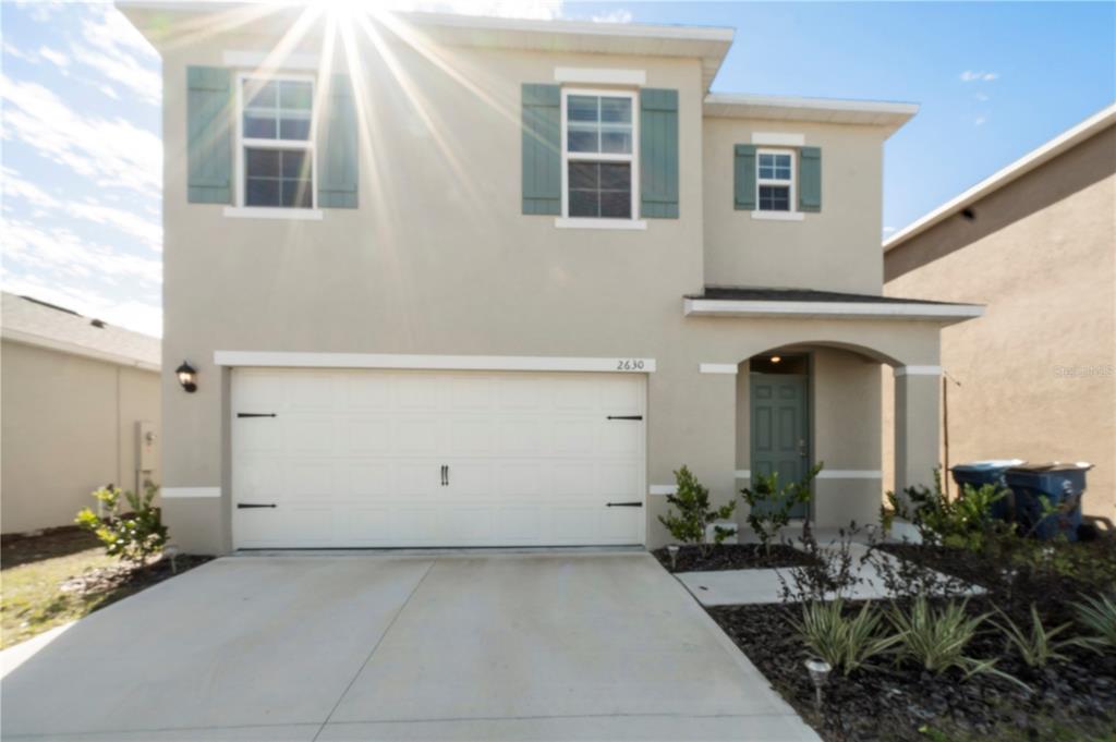 A two-story house with a white garage door, beige stucco exterior, and teal window shutters — 2630 ANGEL FALLS DRIVE, DAVENPORT, FL