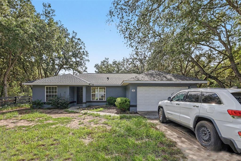 A gray single-story house with a white garage door sits among trees with a car parked — 135 FISHER WAY TRAIL, OCKLAWAHA, FL