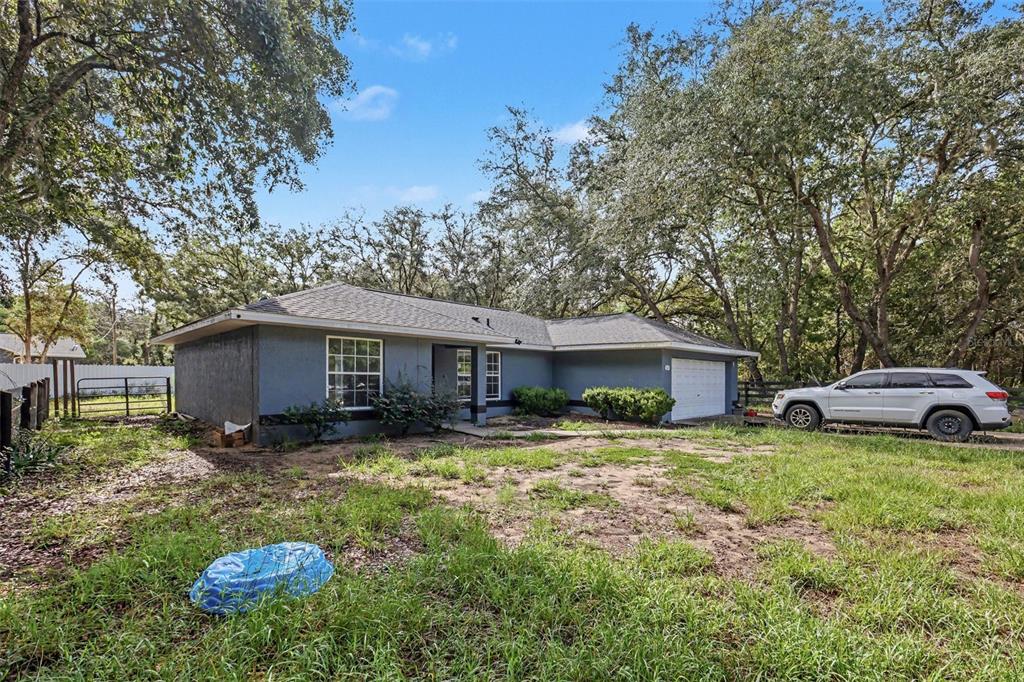 A single-story blue house with a white garage and a large, grassy front yard — 135 FISHER WAY TRAIL, OCKLAWAHA, FL