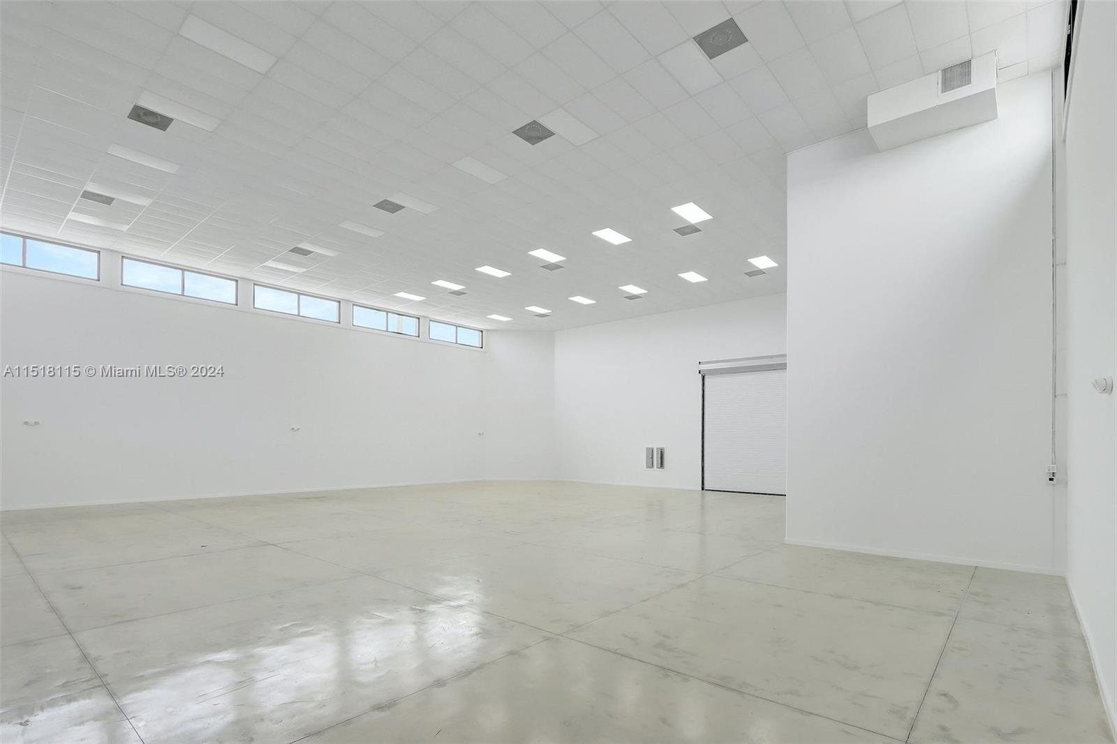 An empty, white-walled industrial space features a high drop ceiling and a roll-up door — 235 NE 67th St, Miami FL 33138, MIAMI, FL