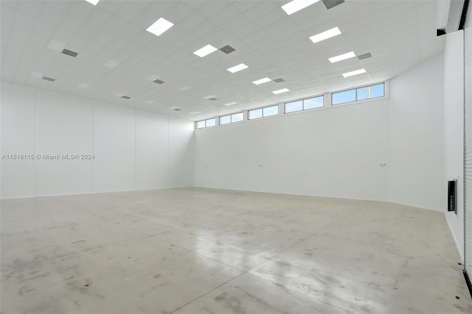 An empty, white-walled commercial space features a drop ceiling with recessed lighting and concrete flooring — 235 NE 67th St, Miami FL 33138, MIAMI, FL