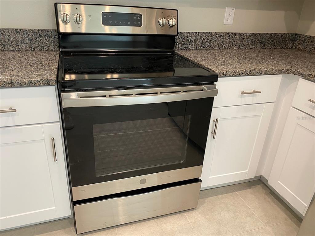 A stainless steel electric range is situated between white cabinets and granite countertops — 8533 REEDVILLE STREET, NEW PORT RICHEY, FL