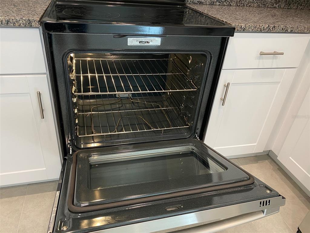 A kitchen features a stainless steel oven with an open door and white cabinetry — 8533 REEDVILLE STREET, NEW PORT RICHEY, FL