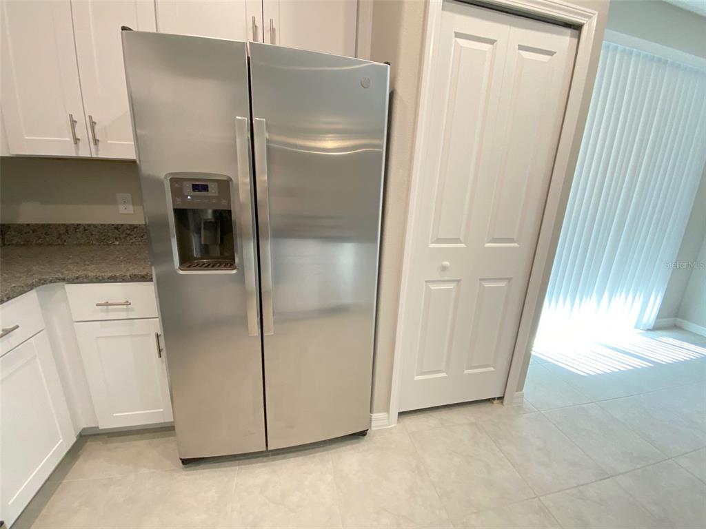 A stainless steel side-by-side refrigerator stands in a kitchen with white cabinets and tile flooring — 8533 REEDVILLE STREET, NEW PORT RICHEY, FL