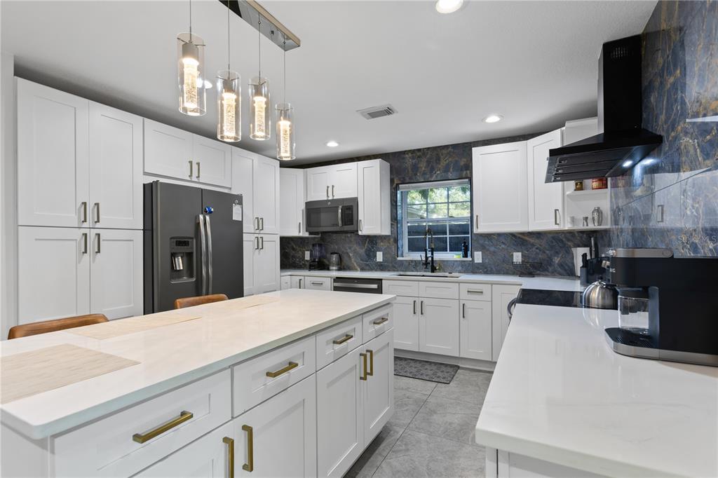 A modern kitchen features white cabinets, a large island, and a dark marble-patterned backsplash — 6822 S WALL STREET, TAMPA, FL