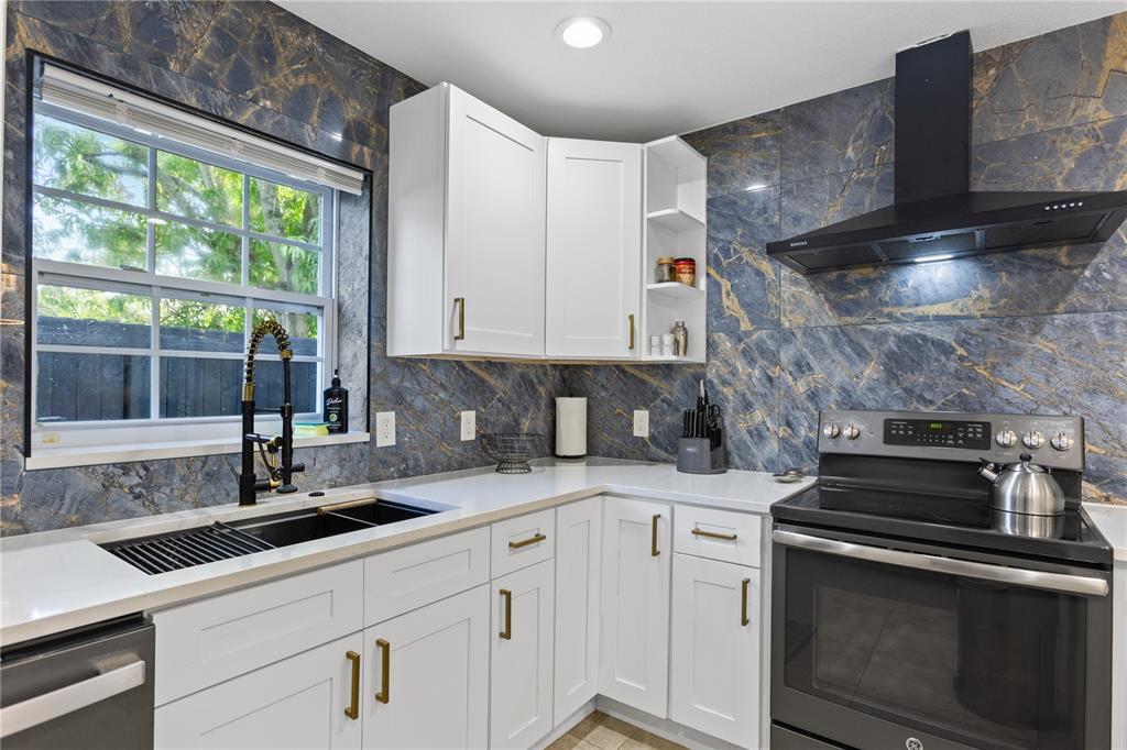 A kitchen features white cabinets, a dark marble backsplash, and a black range hood — 6822 S WALL STREET, TAMPA, FL