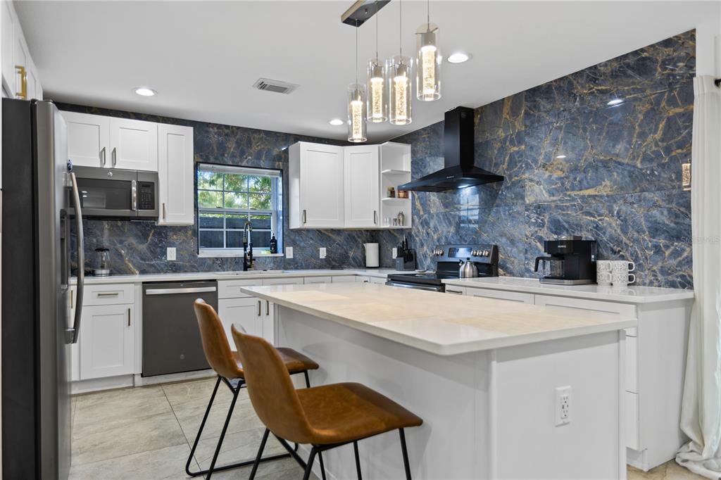 A modern kitchen features white cabinetry, a large island, and blue marble-patterned tile walls — 6822 S WALL STREET, TAMPA, FL