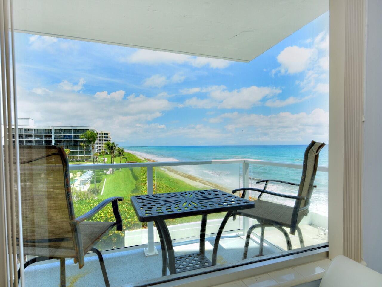 A balcony with a table and two chairs overlooks the ocean and a coastal building — 3450 S Ocean Boulevard # 308, Palm Beach FL 33480, PALM BEACH, FL