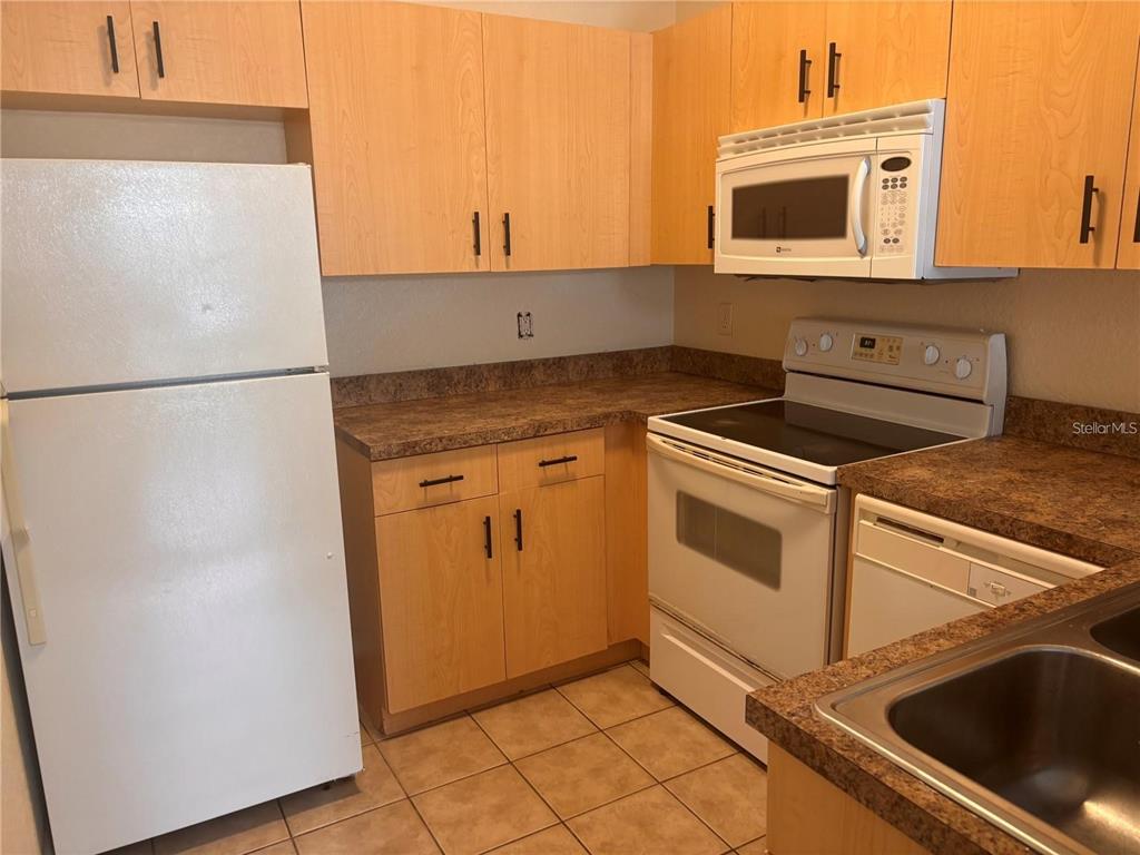 A kitchen features light wood cabinets, white appliances, and brown laminate countertops with tile flooring — 21102 INDIAN CREEK DRIVE, POINCIANA, FL