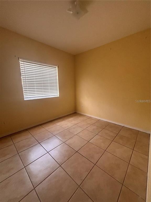 An empty bedroom features light yellow walls, a window with blinds, and tiled flooring — 21102 INDIAN CREEK DRIVE, POINCIANA, FL