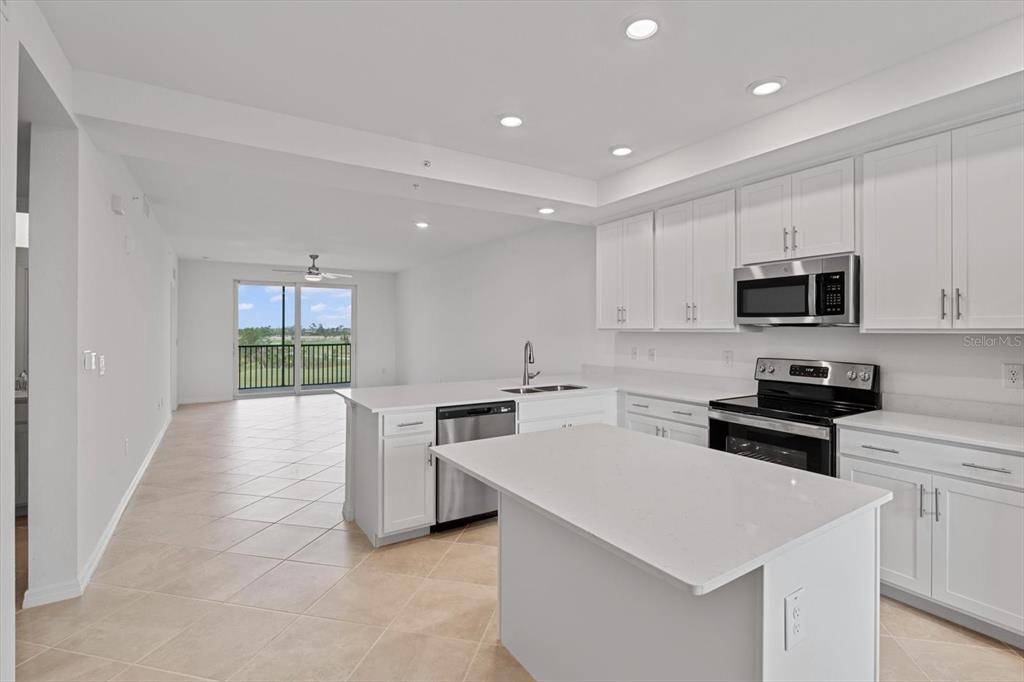 A modern kitchen with white cabinets, stainless steel appliances, and an island overlooks a balcony — 12180 WELLEN GOLF STREET UNIT 305, VENICE, FL