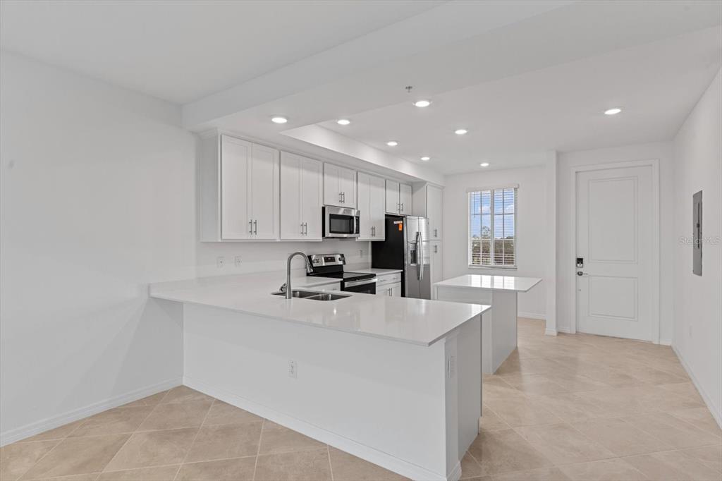 A modern kitchen features white cabinets, quartz countertops, a center island, and tile flooring — 12180 WELLEN GOLF STREET UNIT 305, VENICE, FL