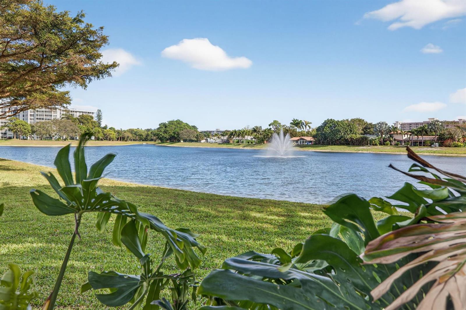 A view of a lake with a fountain, surrounded by grass, trees, and residential buildings — 3200 N Course Lane # 116, Pompano Beach FL 33069, POMPANO BEACH, FL