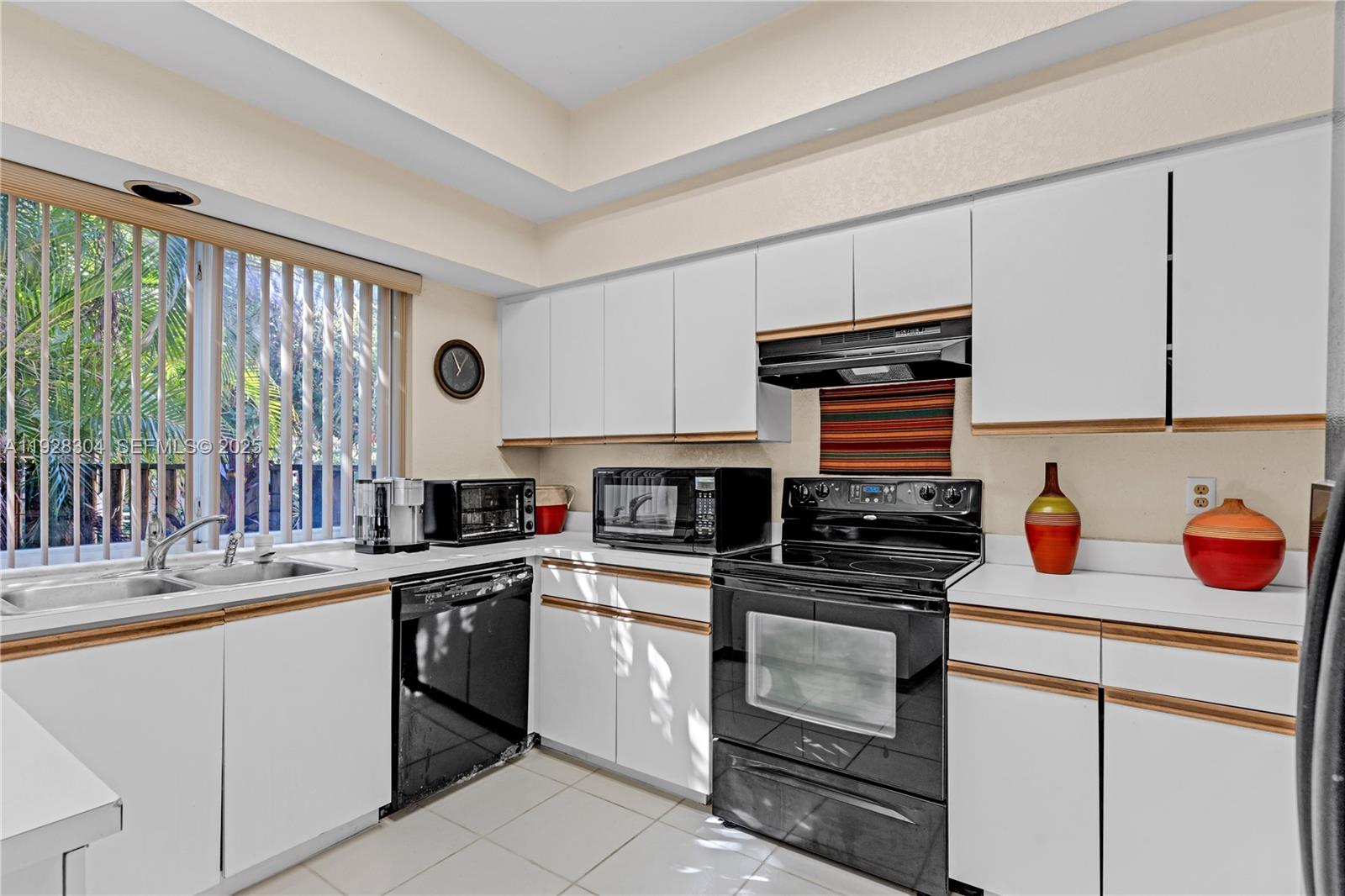 A kitchen features white cabinets with wood trim, black appliances, and a window with blinds — 10132 NW 4th St, Plantation FL 33324, PLANTATION, FL