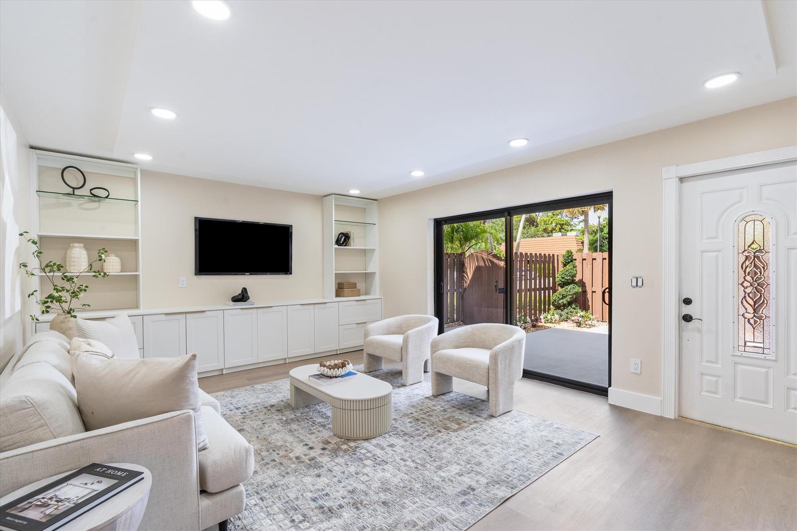 A living room features a white built-in media unit, light flooring, and a sliding glass door — 825 Center Street # 49d, Jupiter FL 33458, JUPITER, FL