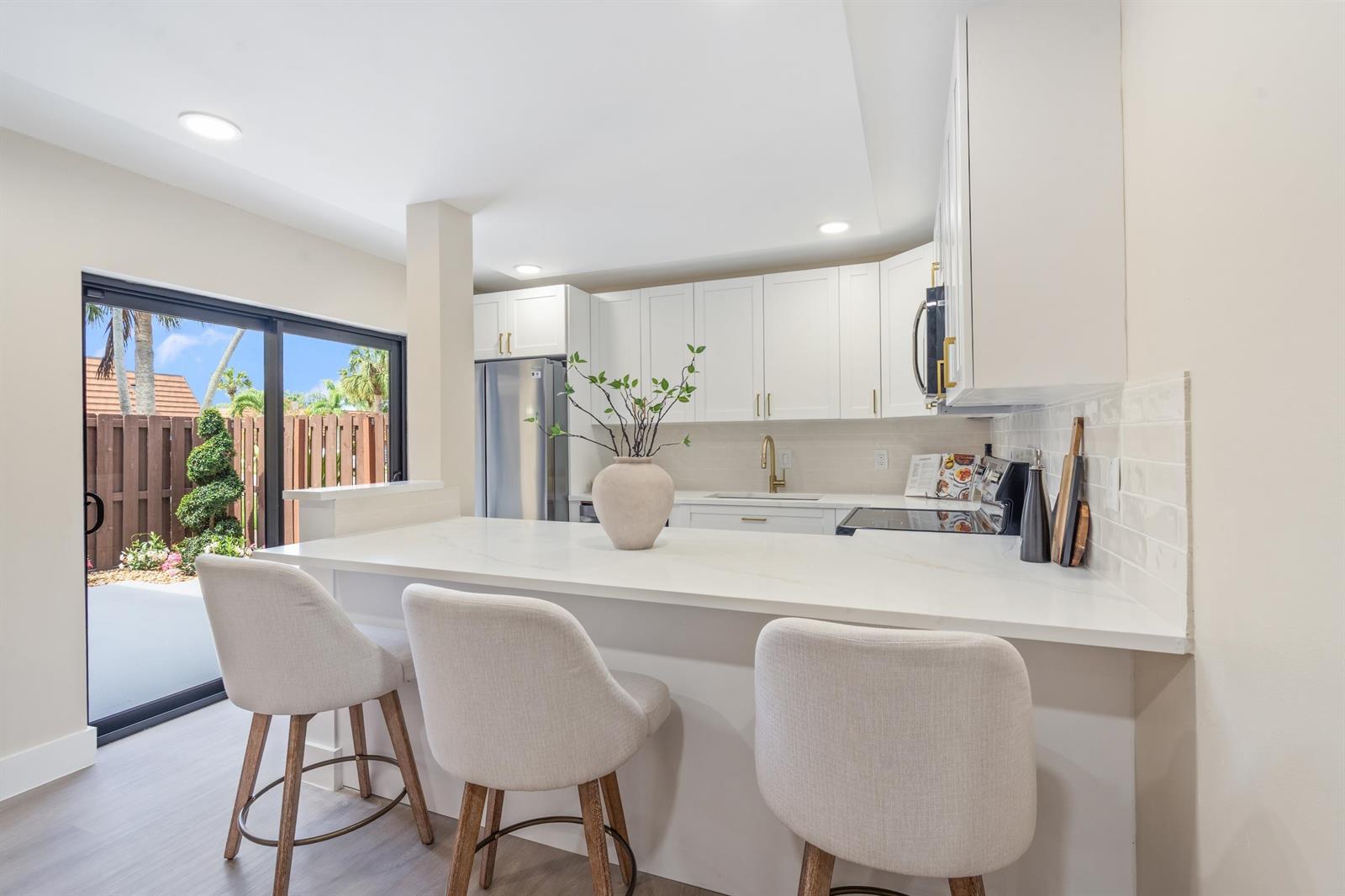 A modern kitchen features white cabinetry, a quartz breakfast bar, and a sliding glass door — 825 Center Street # 49d, Jupiter FL 33458, JUPITER, FL