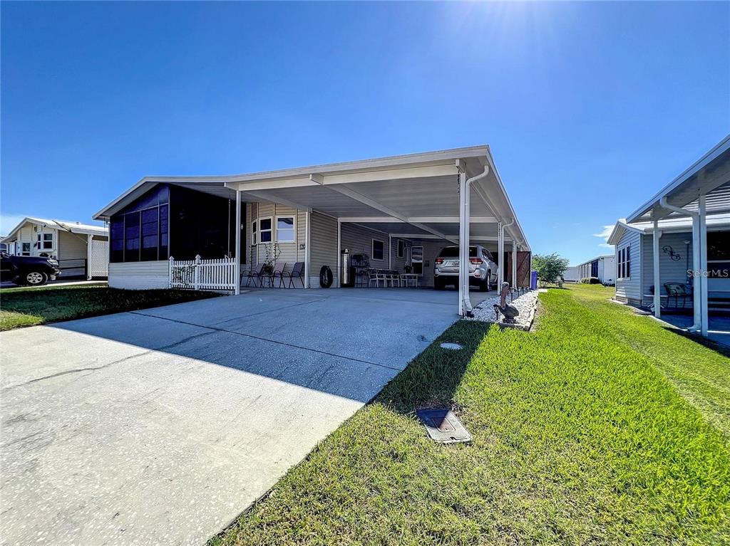 A single-story manufactured home features a large attached carport and a concrete driveway — 1785 QUAIL HILL DRIVE, LAKELAND, FL