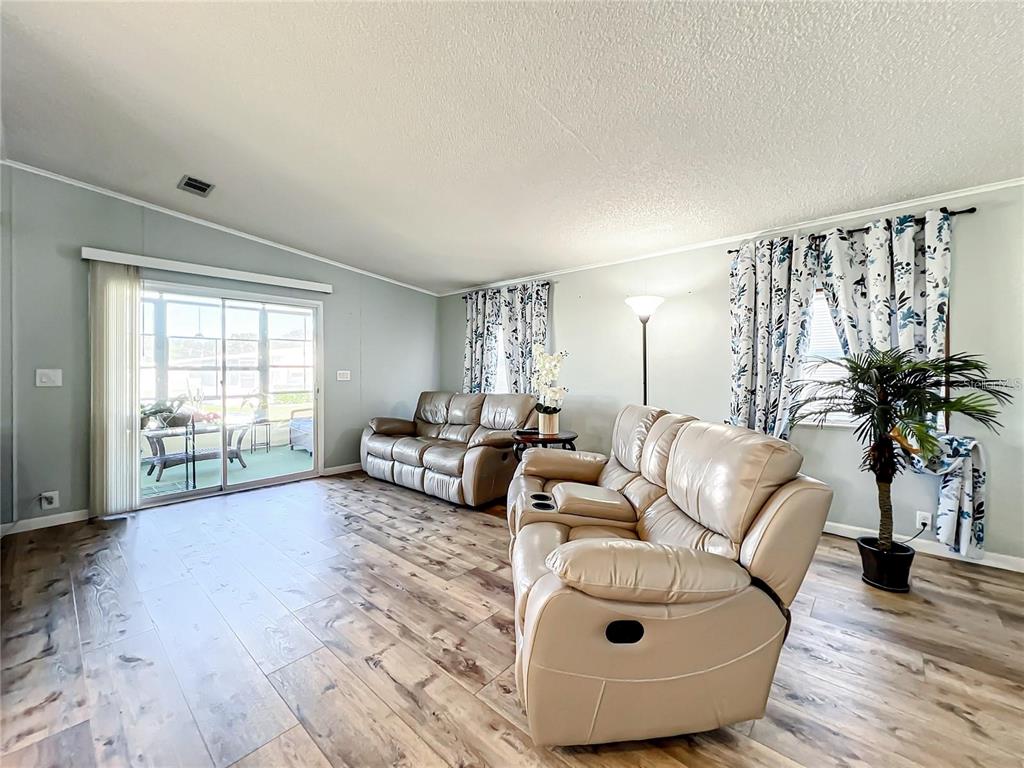 A living room features light-colored leather sofas, wood-look flooring, and a sliding glass door — 1785 QUAIL HILL DRIVE, LAKELAND, FL