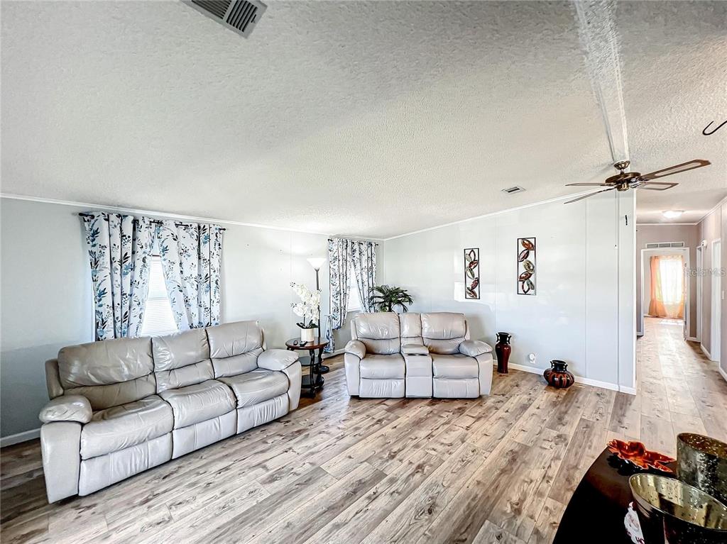A living room features light-colored leather sofas, wood-look flooring, and floral curtains — 1785 QUAIL HILL DRIVE, LAKELAND, FL