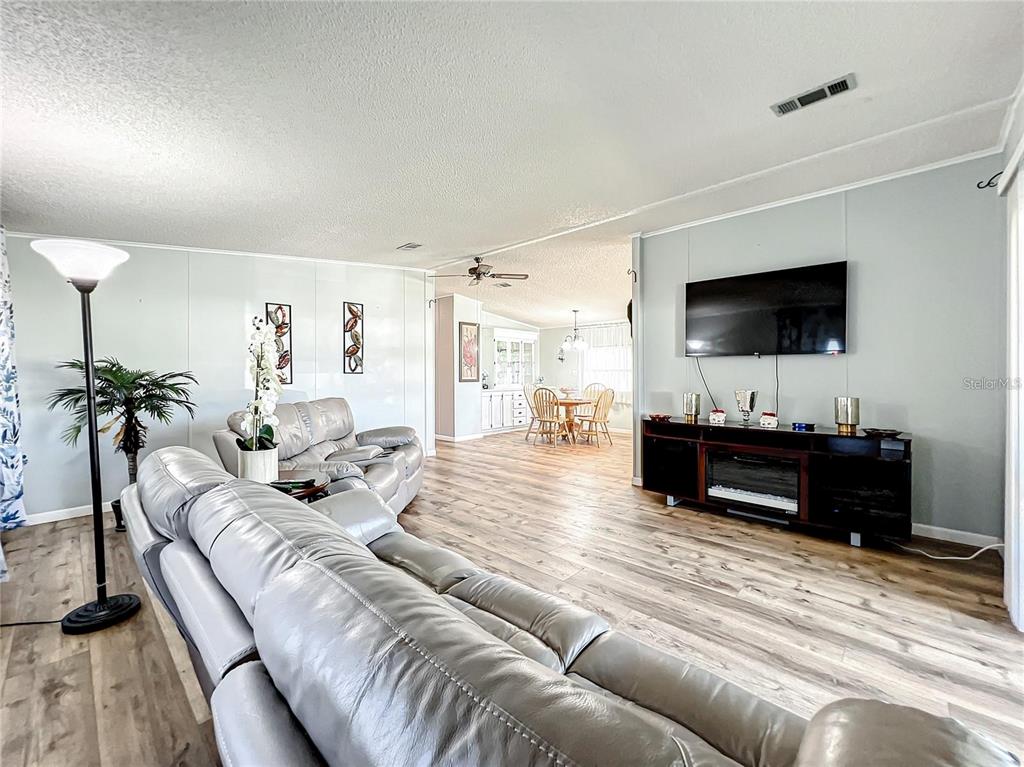 A living room with light wood-look flooring, a grey leather sofa, and a wall-mounted television — 1785 QUAIL HILL DRIVE, LAKELAND, FL