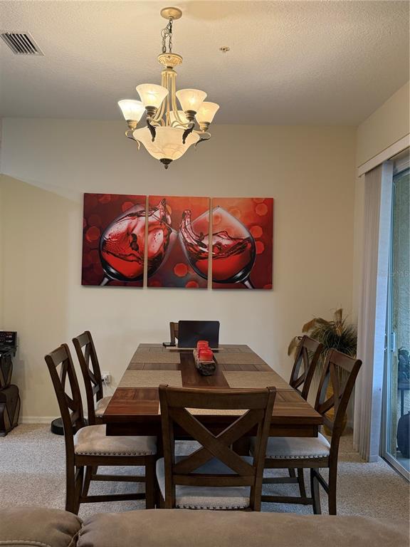 A dining room features a wooden table, six chairs, a chandelier, and wine-themed wall art — 3625 SQUARE WEST LANE UNIT 4, SARASOTA, FL