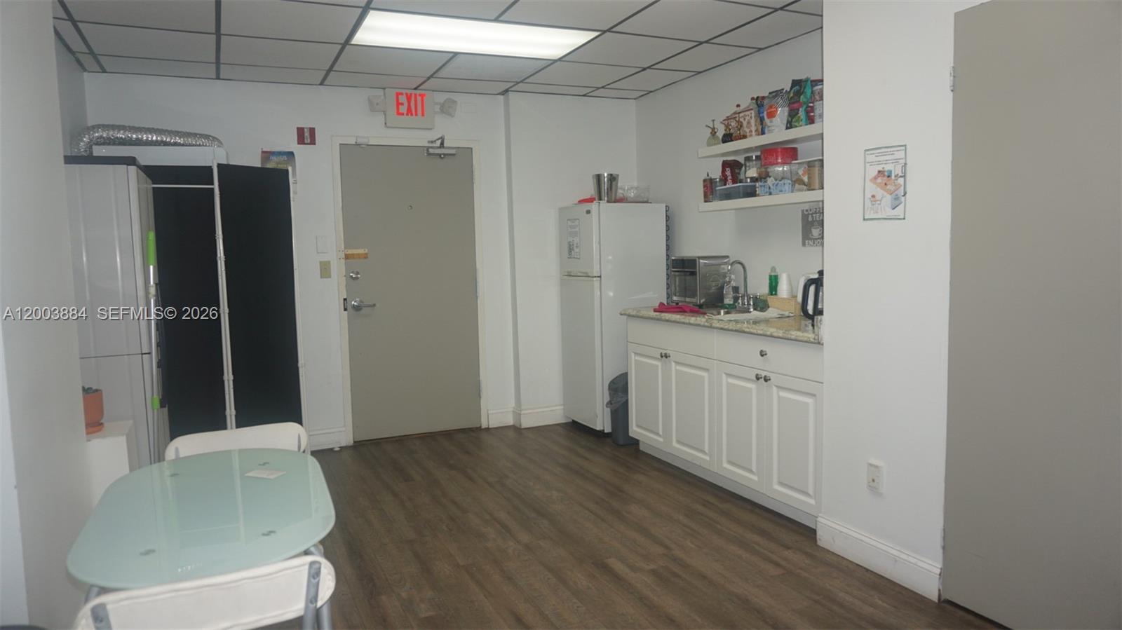 A small break room features a kitchenette, a dining table, and a gray exit door — 1250 E Hallandale Beach Blvd, Hallandale Beach FL 33009, HALLANDALE BEACH, FL