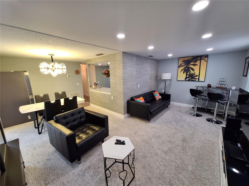 A living room and dining area featuring black leather furniture, gray carpeting, and recessed lighting — 4022 BEAVER LANE UNIT 1000G, PORT CHARLOTTE, FL