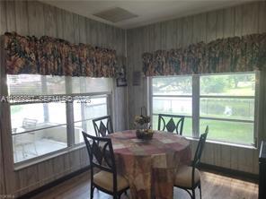 A dining area features a round table with four chairs, wood-paneled walls, and large windows — 1104 Gulf St, Moore Haven FL 33471, MOORE HAVEN, FL