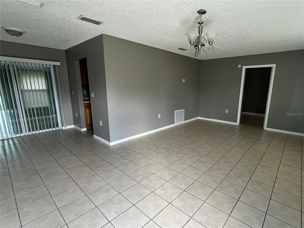 An empty room features gray walls, tiled flooring, a chandelier, and a sliding glass door — 2603 SW 152ND LANE, OCALA, FL