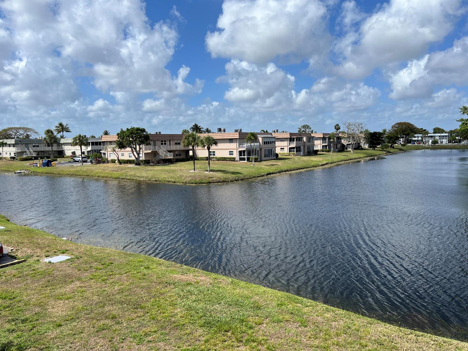 A view of multi-story apartment buildings situated along the edge of a pond — 192 Monaco D, Delray Beach FL 33446, DELRAY BEACH, FL
