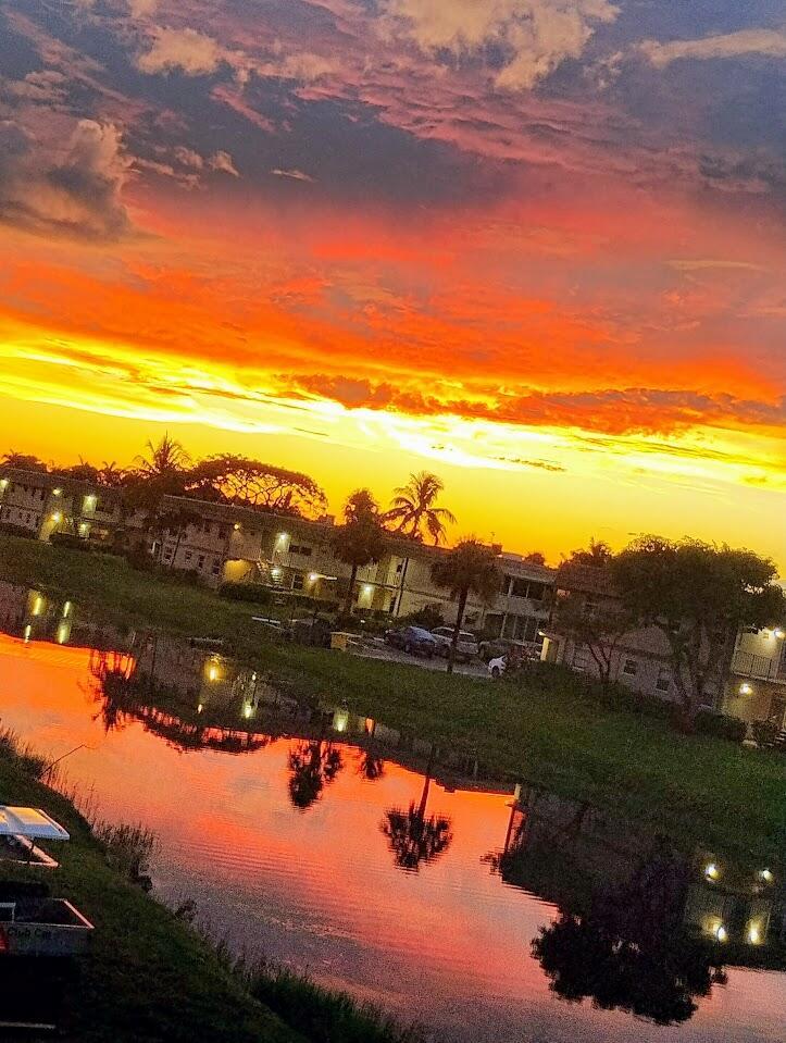 A vibrant sunset reflects over a canal in front of a multi-story apartment complex — 192 Monaco D, Delray Beach FL 33446, DELRAY BEACH, FL