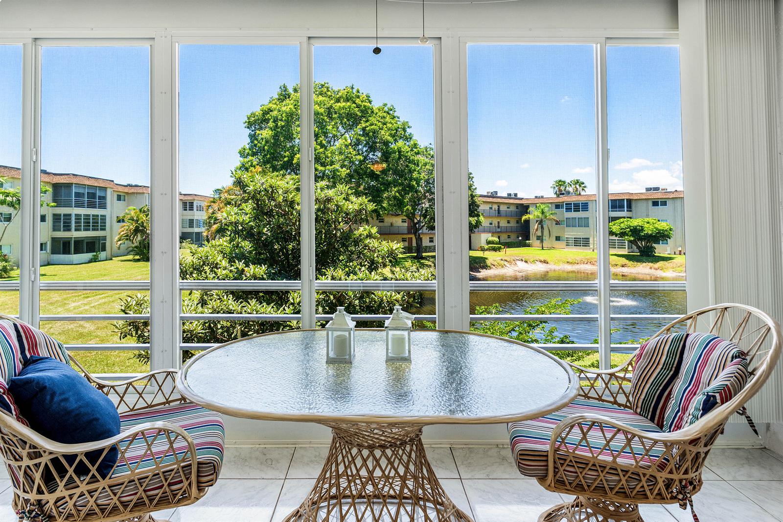 A sunroom features a glass-topped table, wicker chairs, and a view of a pond — 721 Lori Drive # 208, Palm Springs FL 33461, PALM SPRINGS, FL