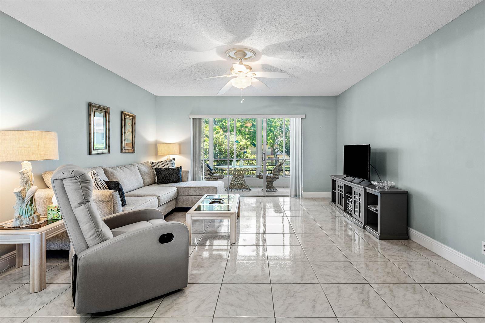 A living room features light blue walls, tile flooring, a sectional sofa, and a balcony — 721 Lori Drive # 208, Palm Springs FL 33461, PALM SPRINGS, FL