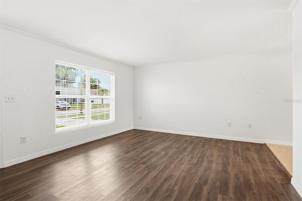 An empty room with white walls, dark wood-look flooring, and a large window — 7826 KNOX LOOP, NEW PORT RICHEY, FL
