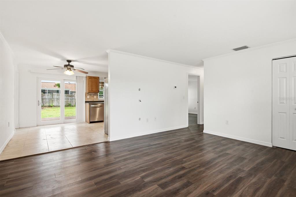 A living room with dark wood-look flooring transitions to a tiled kitchen area with sliding doors — 7826 KNOX LOOP, NEW PORT RICHEY, FL