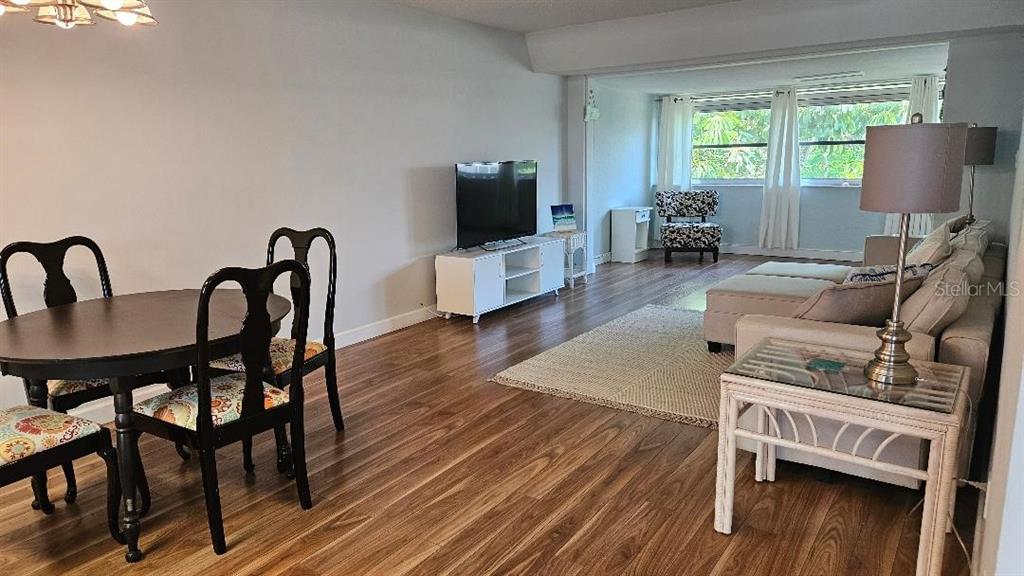 A living and dining area features wood-look flooring, a television console, and neutral furniture — 9950 47TH AVENUE N UNIT 303, ST PETERSBURG, FL