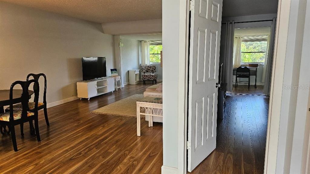 A living room with wood-look flooring and a television leads to a separate bedroom area — 9950 47TH AVENUE N UNIT 303, ST PETERSBURG, FL