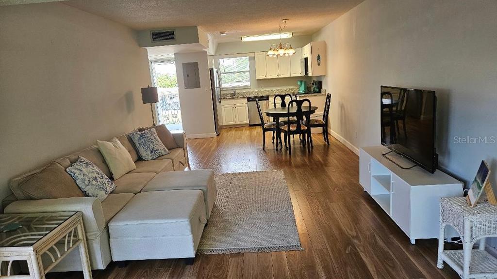 An open-concept living and dining area features light-colored furniture, wood-look flooring, and a kitchen — 9950 47TH AVENUE N UNIT 303, ST PETERSBURG, FL