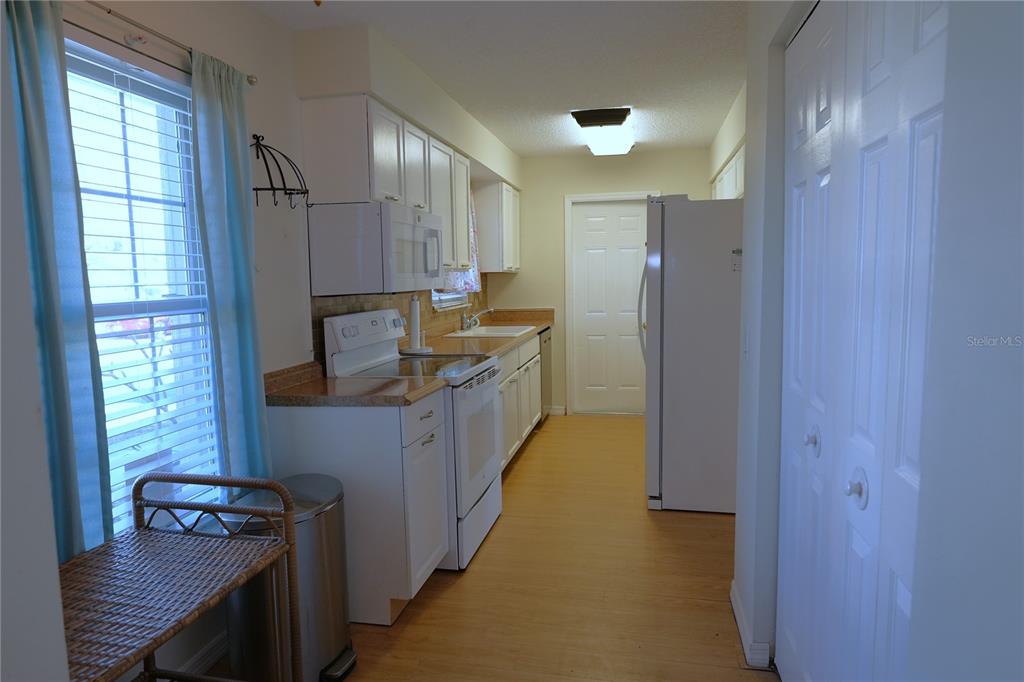 A galley-style kitchen features white cabinets, white appliances, and light wood-look flooring — 3074 PERDUE TERRACE, PUNTA GORDA, FL