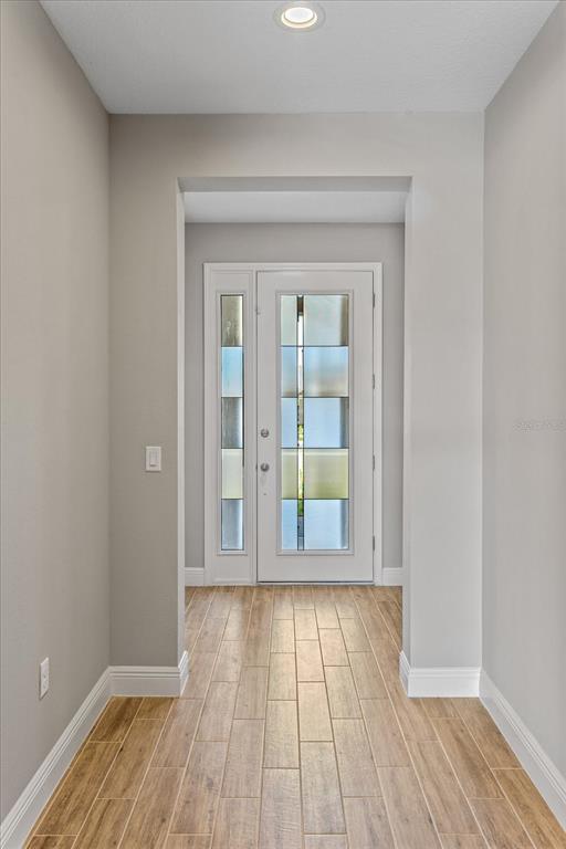 A hallway with light wood-look tile flooring leads to a white front door with glass panels — 17314 WILD DAISY DRIVE, WINTER GARDEN, FL